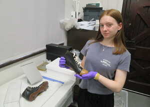 Two people stand in a museum, with exhibits and artifacts displayed in the background.