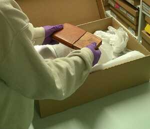 A person wearing purple nitrile gloves holding an object that has been taken out of one of the boxes containing objects from the museum collection